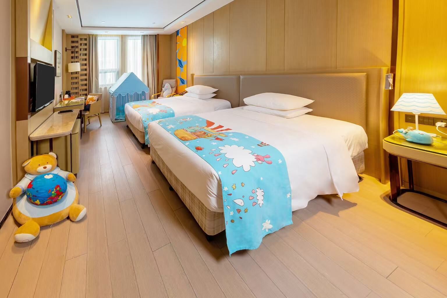 A hotel room with two beds, a TV, a desk, and a teddy bear.