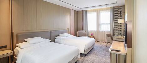 A hotel room with two beds, a desk, a chair, and a TV.