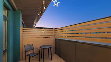 Un balcon avec des lattes en bois, une chaise, une petite table et des guirlandes lumineuses en forme d’étoiles.