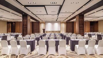 A conference room with rows of tables and chairs, a large screen, and a patterned carpet.