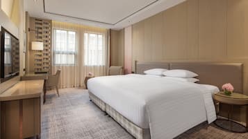Een hotelkamer met een groot bed, een bureau met stoel, een televisie en een kleine tafel met een bloemenvaas.