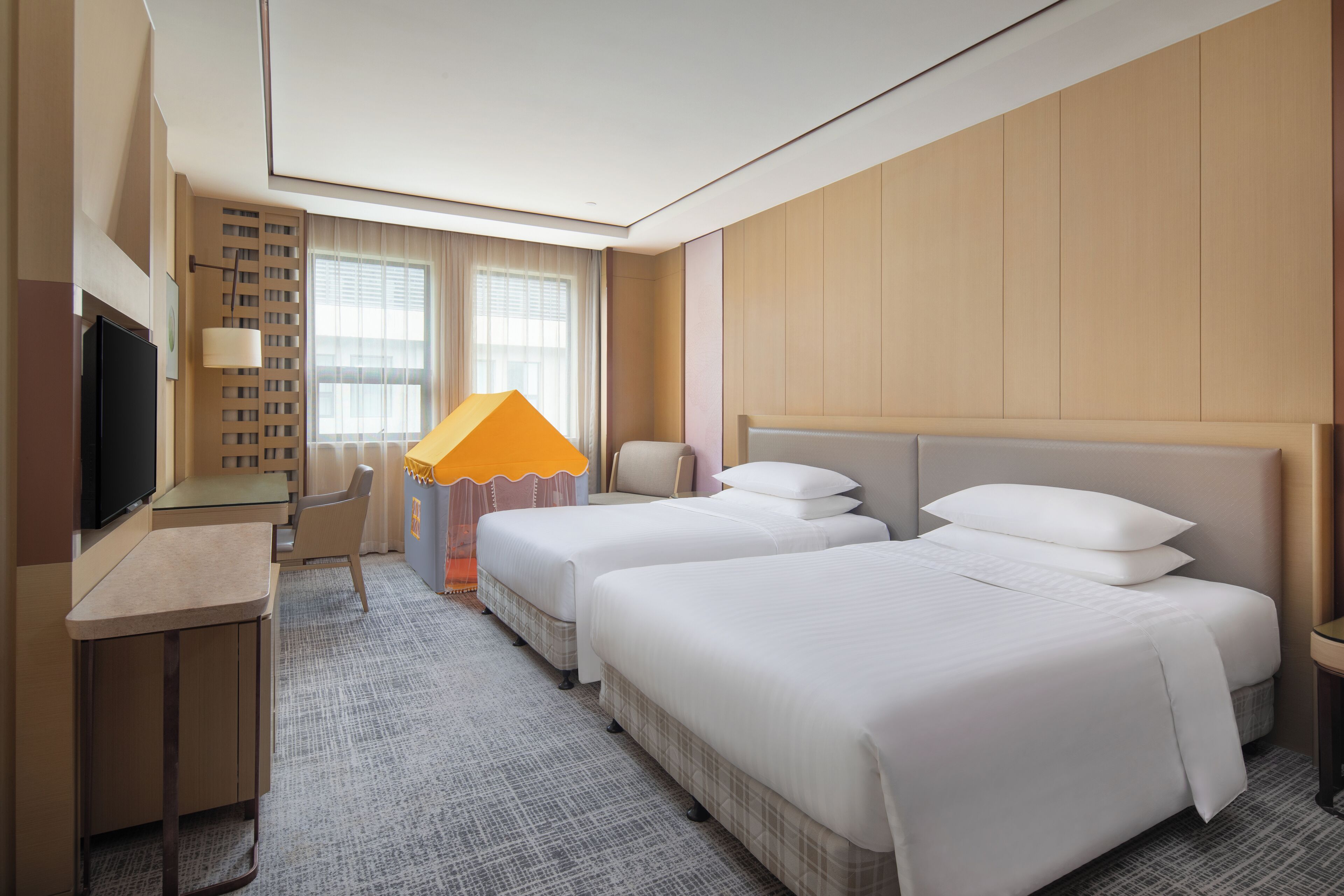 Habitación de hotel con dos camas, un escritorio, un televisor y una ventana con cortinas.