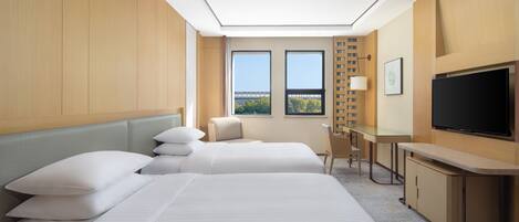 A hotel room with two beds, a desk, a TV, and a window with a view.