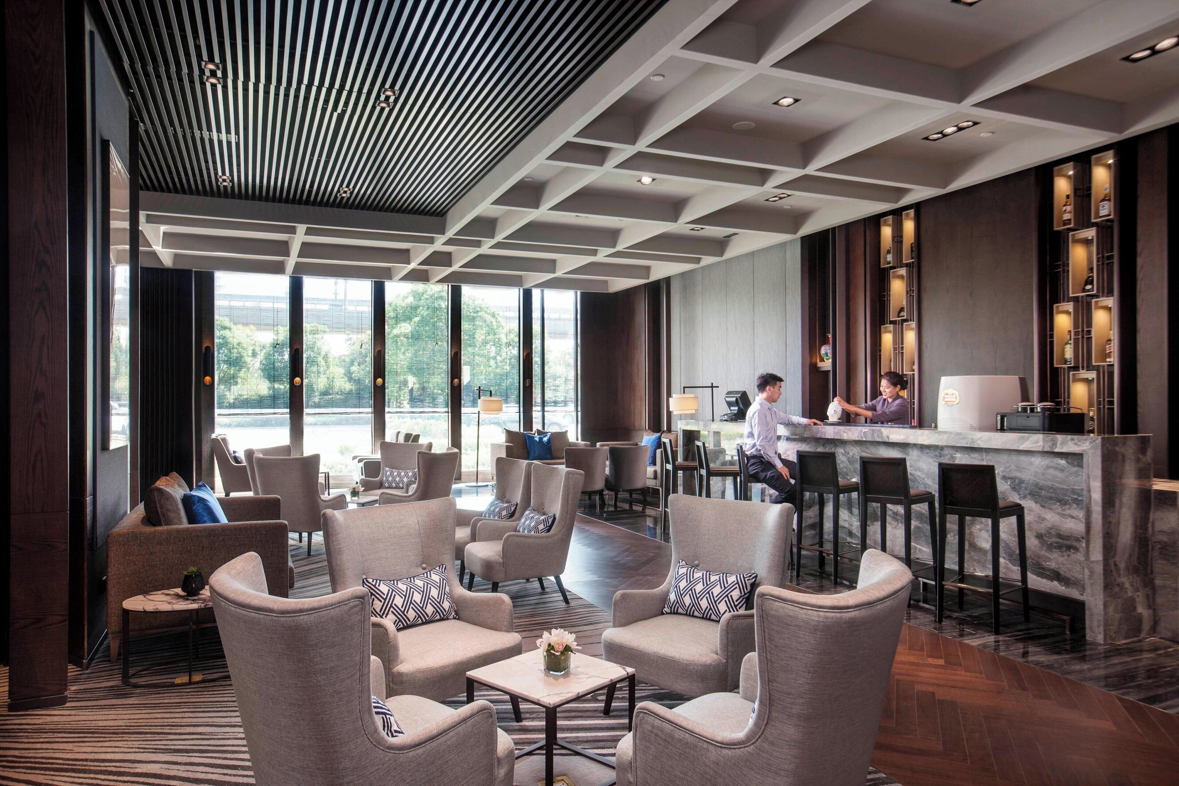 A modern hotel lobby with seating areas, a bar, and large windows offering views.
