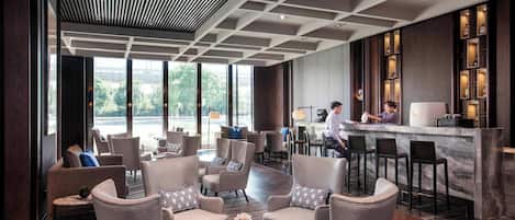 A modern hotel lobby with seating areas, a bar, and large windows offering views.