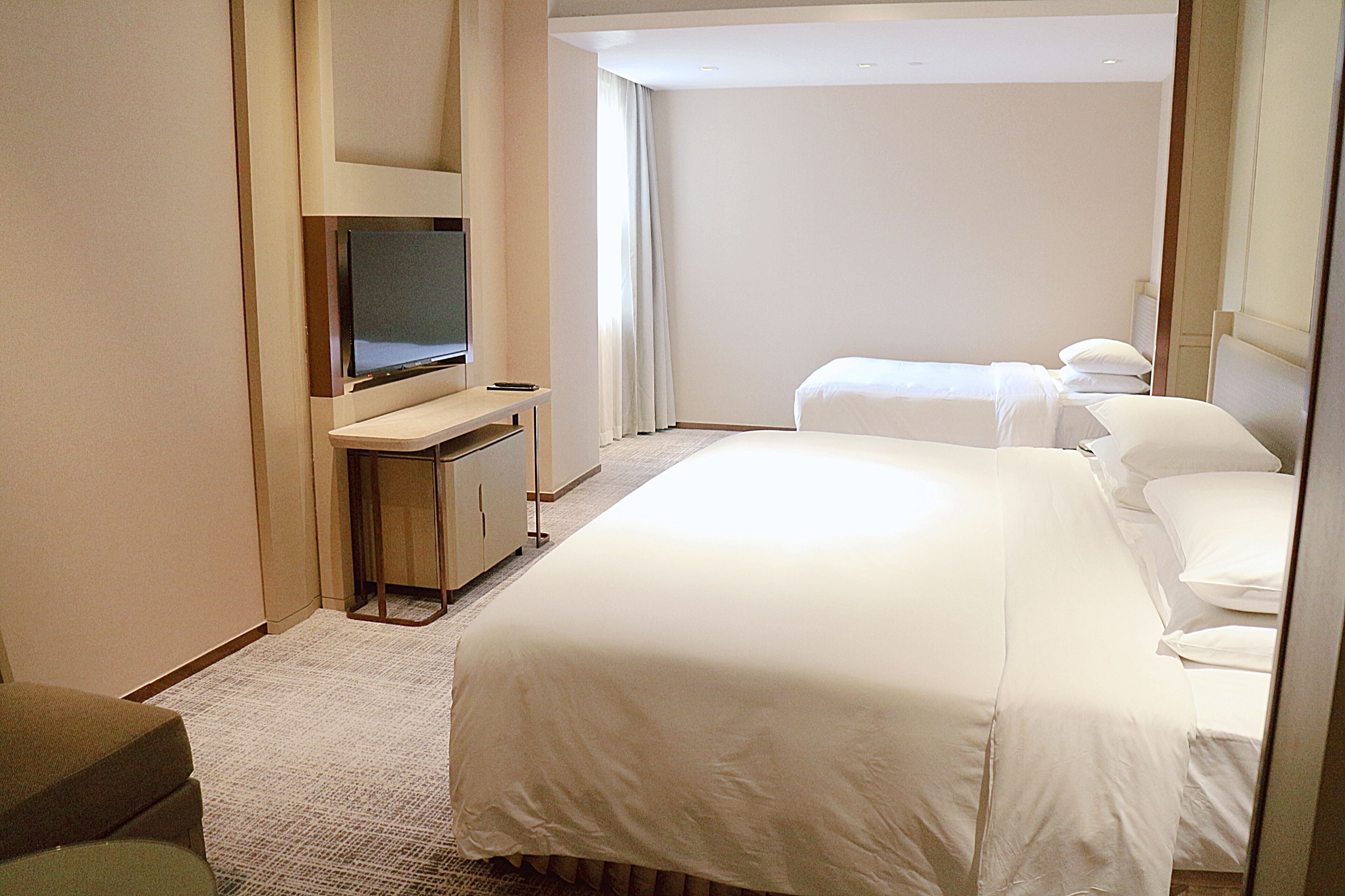 Une chambre d’hôtel avec un lit, une télévision, un bureau et une fenêtre avec des rideaux.