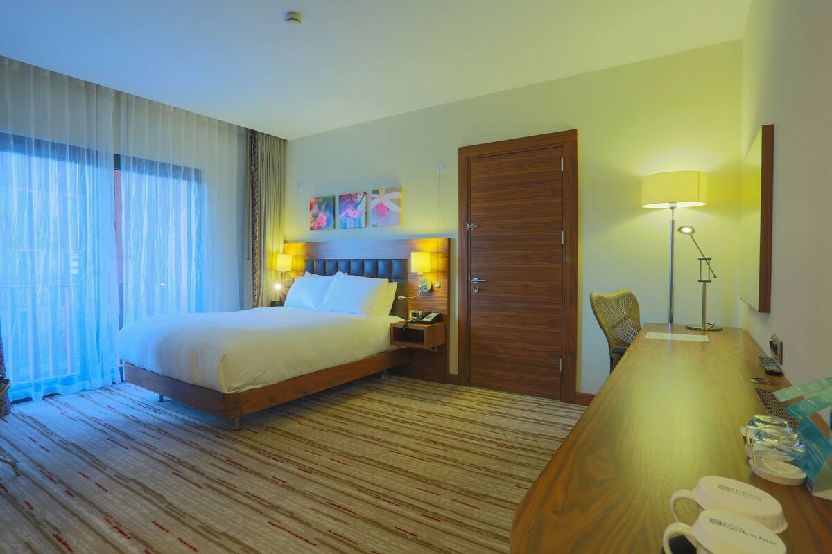 Habitación de hotel con una cama grande, un escritorio con lámpara, una silla y una puerta.