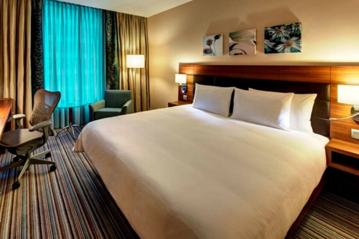 Una habitación de hotel con una cama grande, un escritorio con silla, un televisor y una ventana con cortinas.