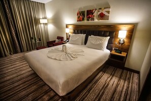 Hotelkamer met een groot bed, een houten hoofdbord, een nachtkastje met een klok, een rode stoel, een lamp en een muur met kunstwerken.