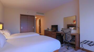 A hotel room with two beds, a desk with a computer, a chair, a TV, and a mirror.