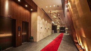 Un moderno vestíbulo de hotel con alfombra roja, paneles de madera e iluminación empotrada en el techo.