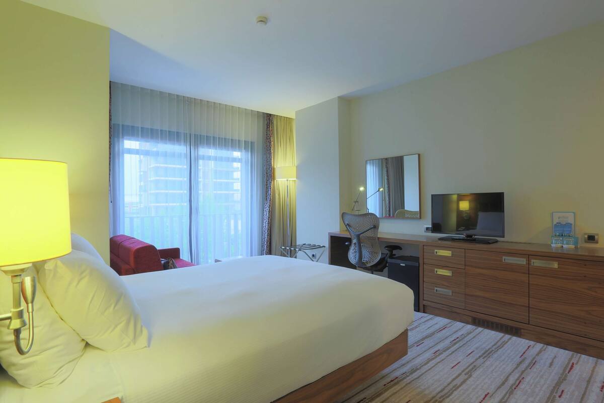 Habitación de hotel con una cama grande, un escritorio con silla, un televisor y un espejo en la pared.