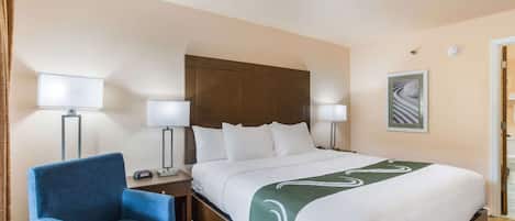 Una habitación de hotel con una cama grande, dos lámparas de noche, un sillón azul y un cuadro en la pared.