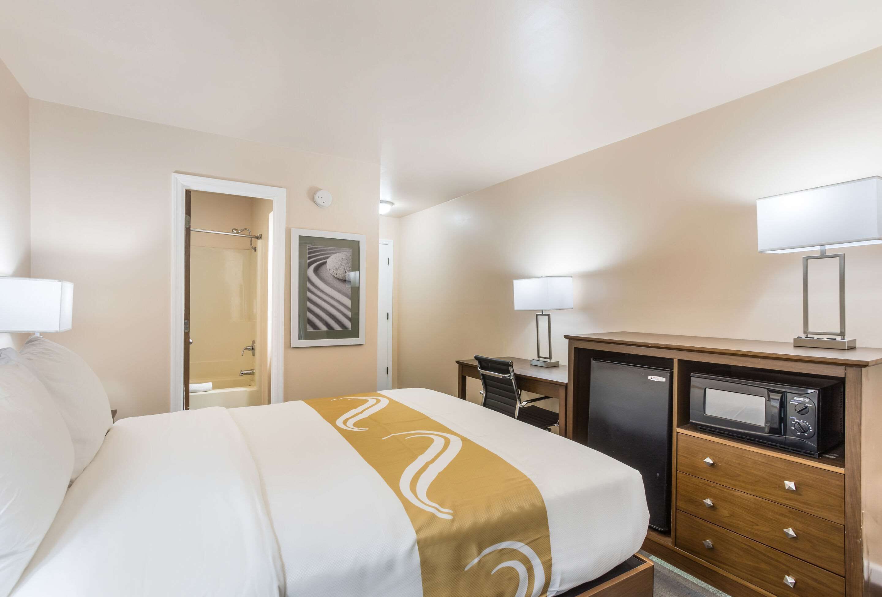 Ein Hotelzimmer mit Bett, Schreibtisch, Mikrowelle und Kommode.