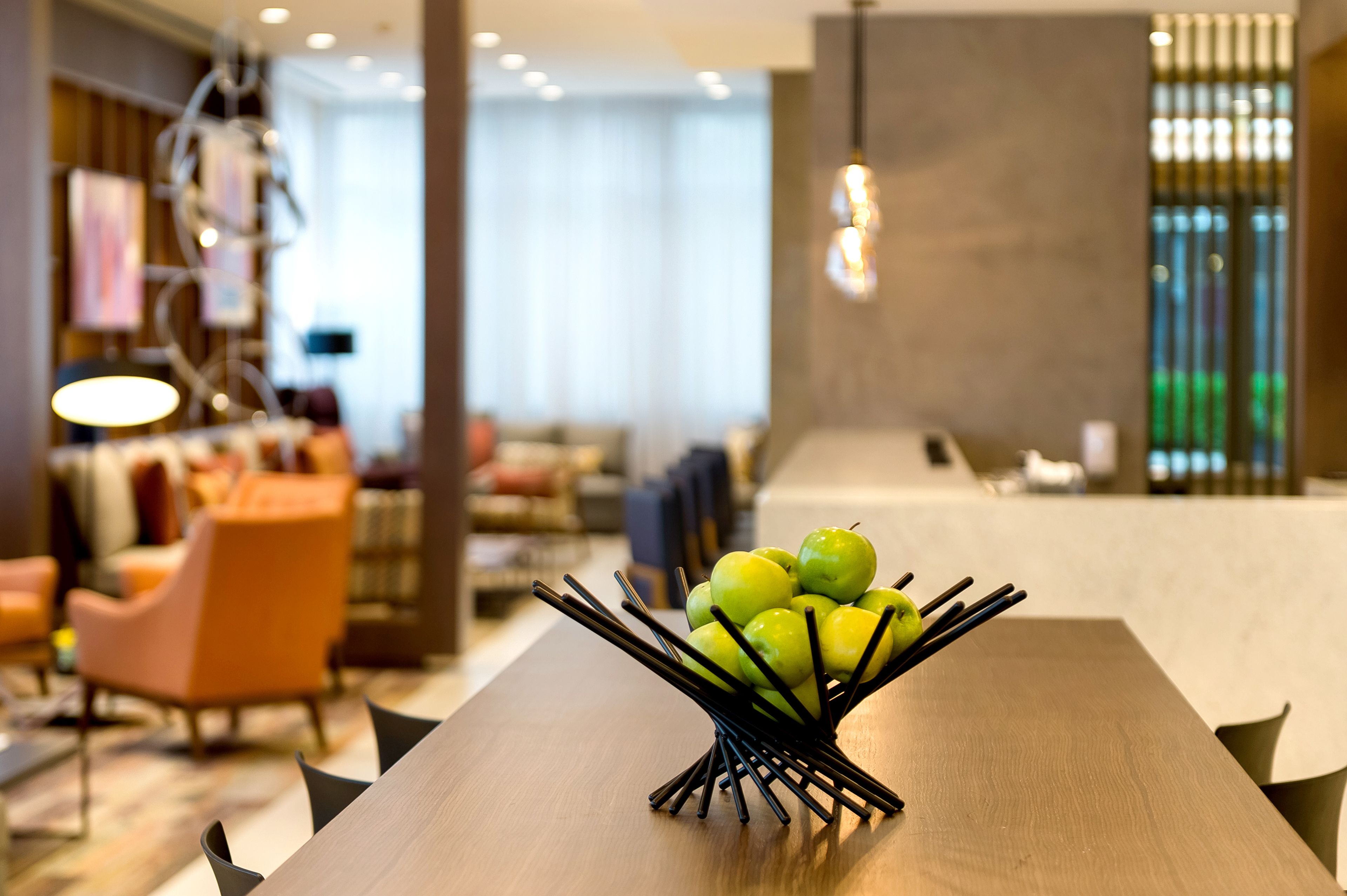 Un espace repas moderne avec une table en bois, un saladier rempli de pommes vertes et des meubles contemporains.