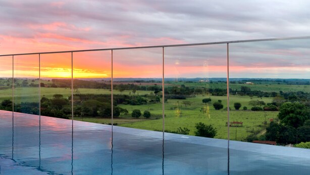 A glass railing overlooking a landscape with a sunset.