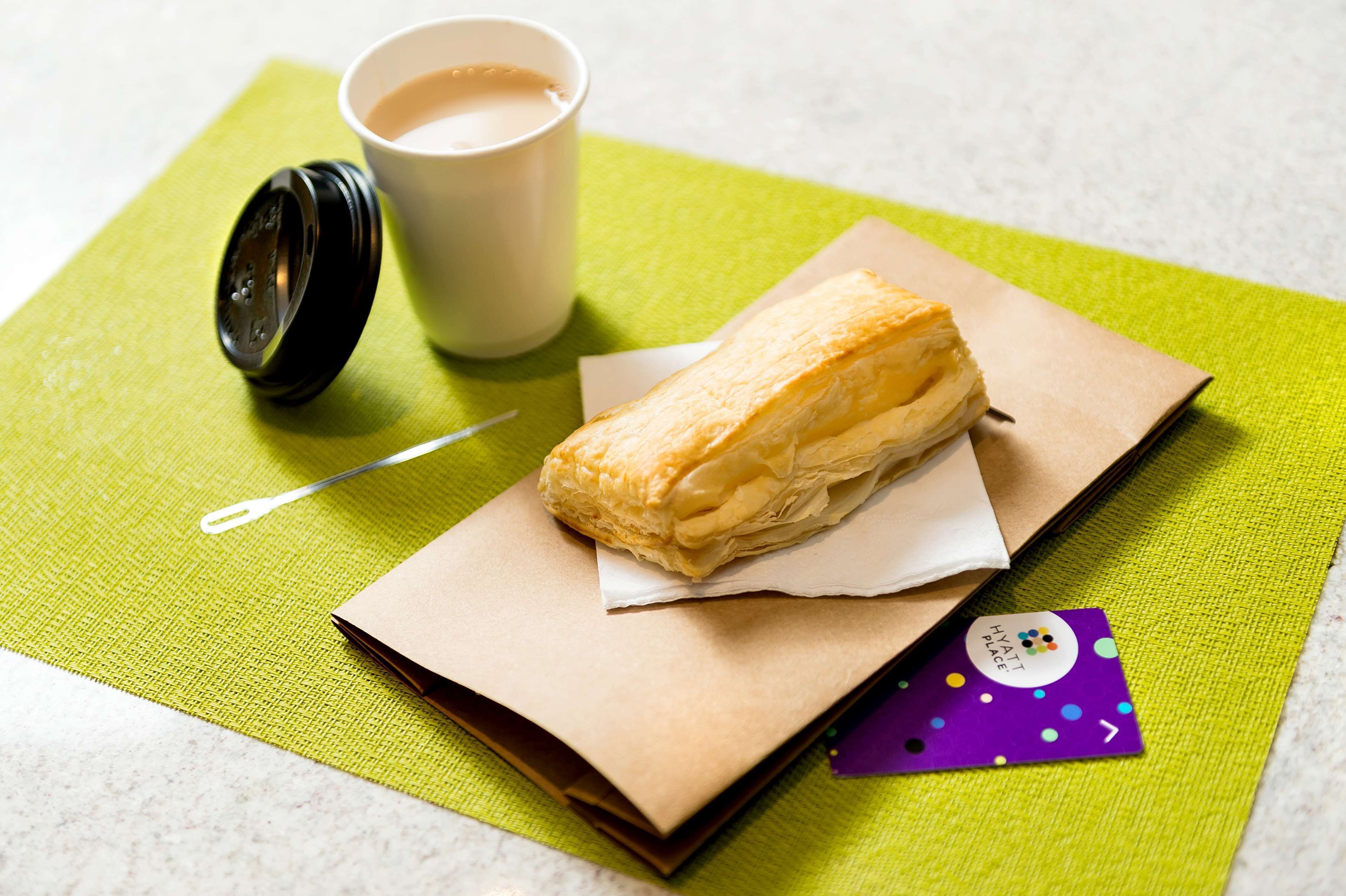 A pastry on a napkin, a cup of coffee, and a hotel card on a green tablecloth.