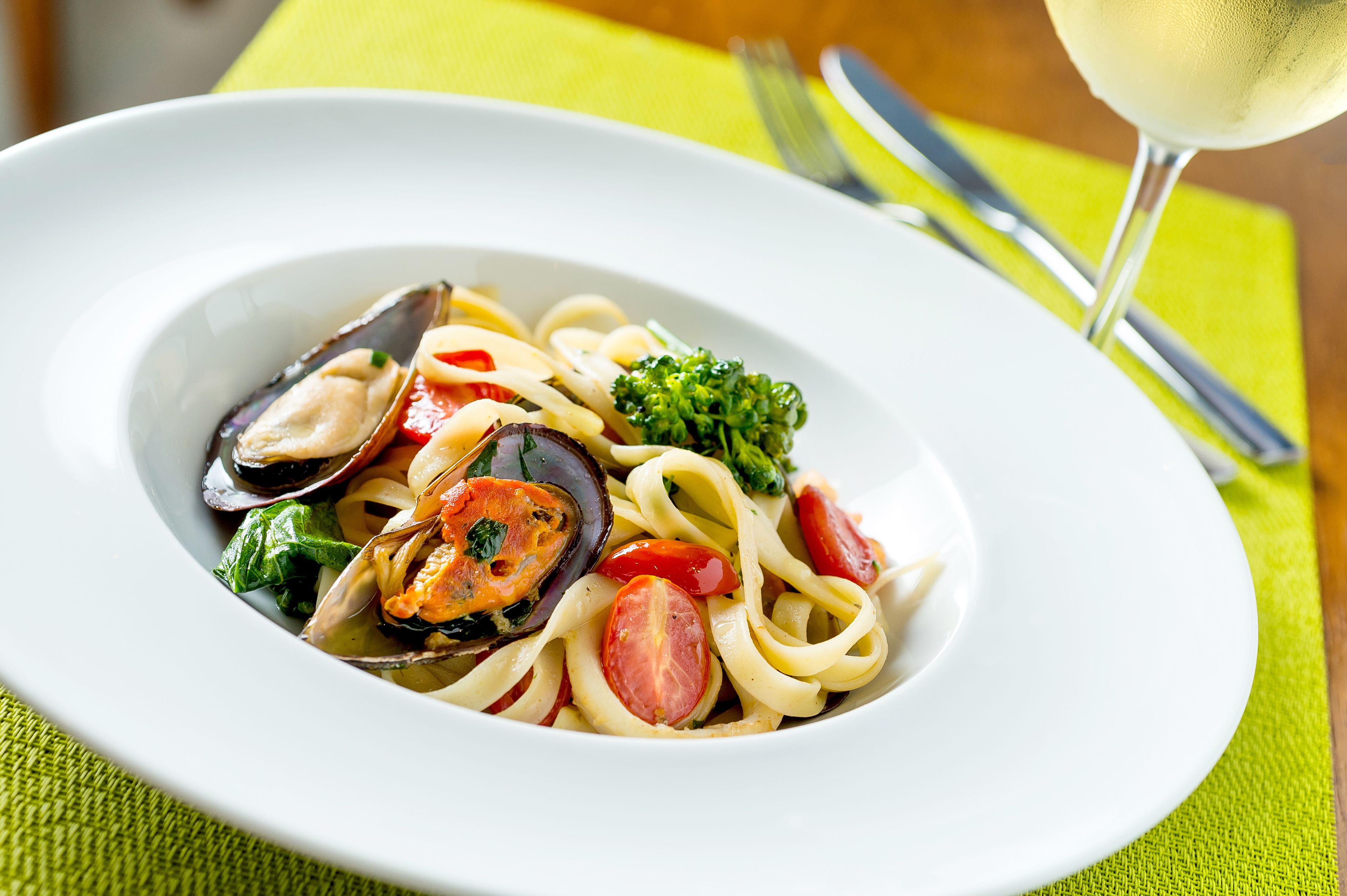 A plate of pasta with mussels, tomatoes, and broccoli.