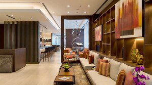 A modern hotel lobby with a reception desk, seating area, and a bar.