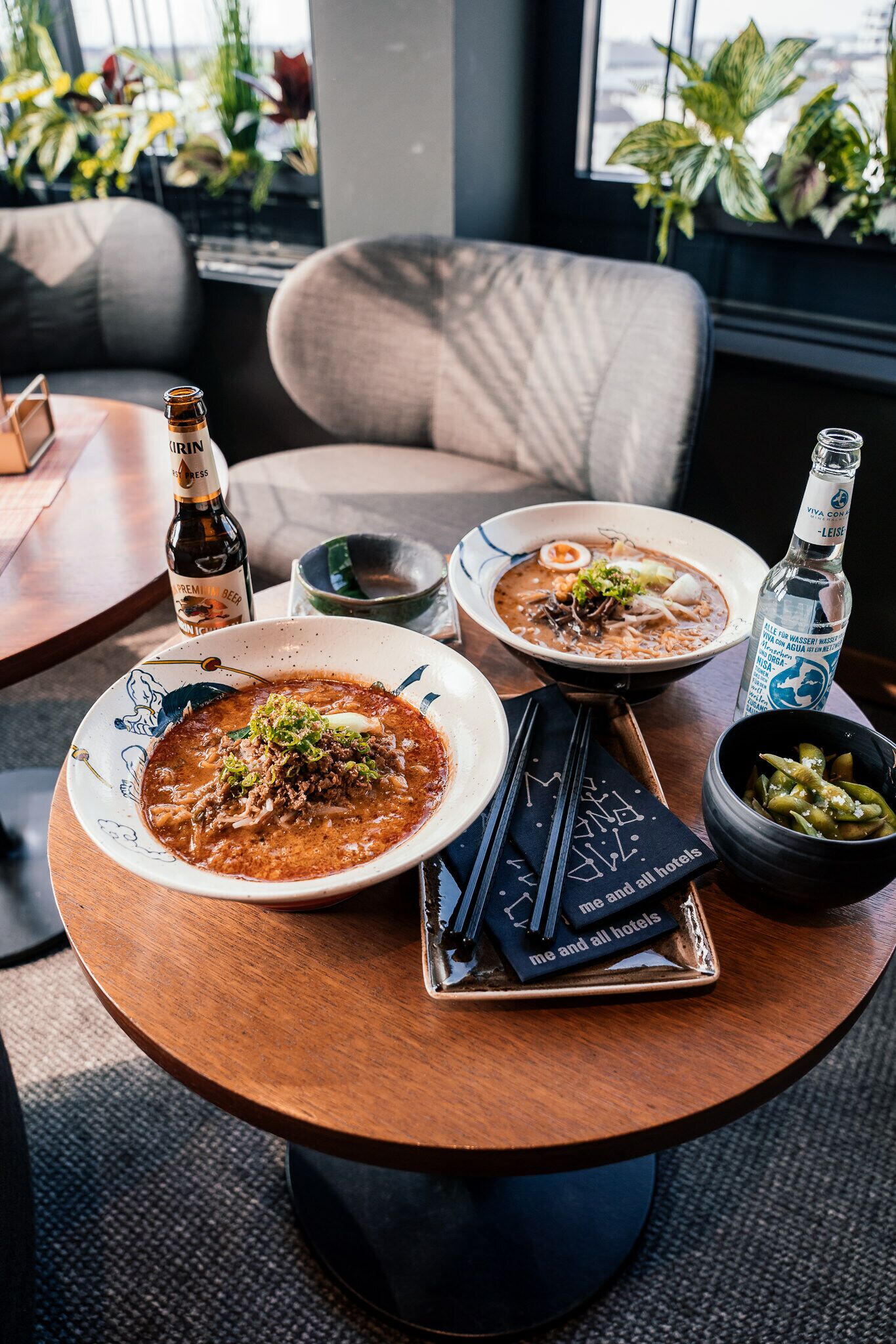 A dining table with two bowls of soup, a bottle of beer, chopsticks, and a menu.