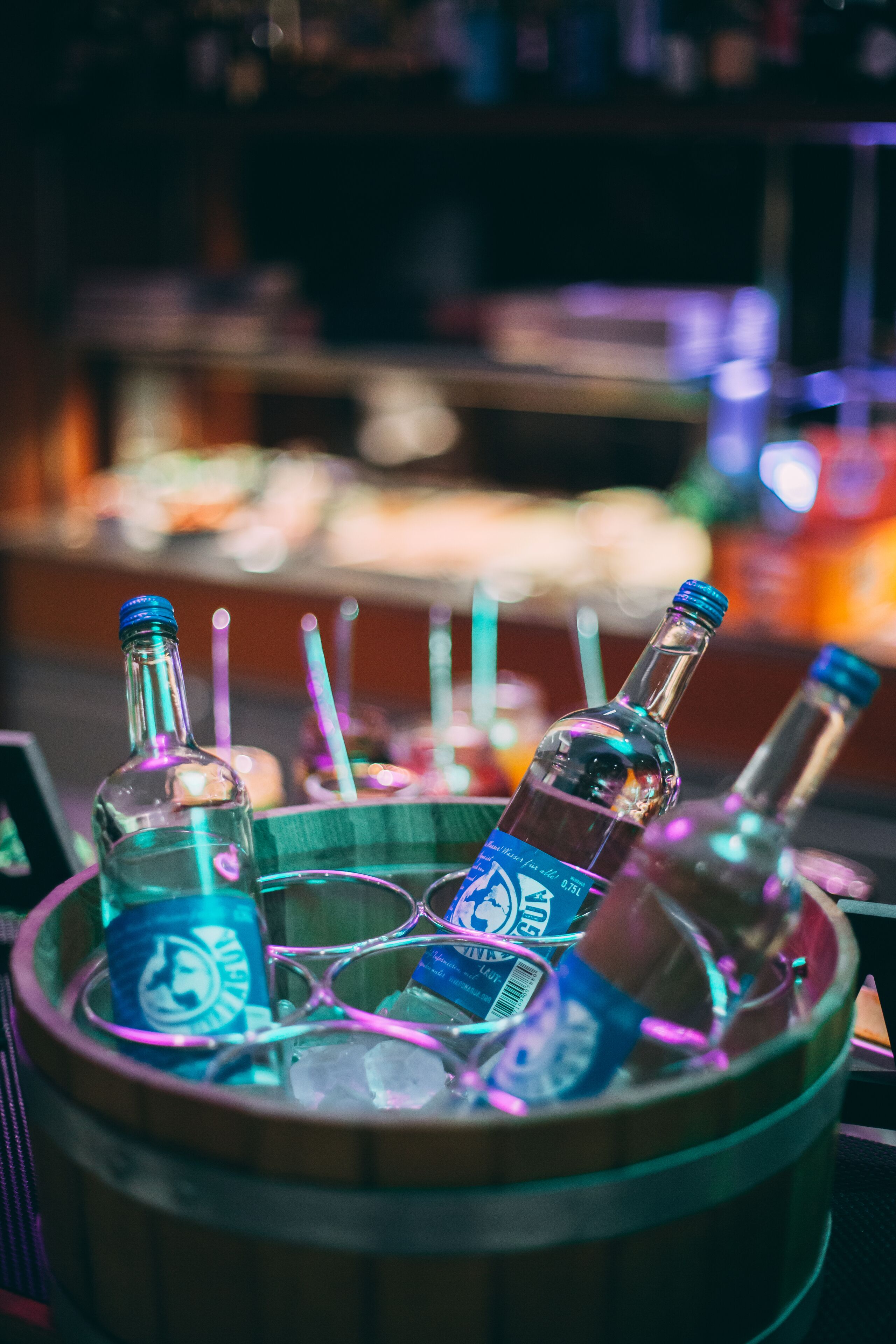 A wooden barrel filled with bottles of alcohol and glasses, likely in a bar setting.