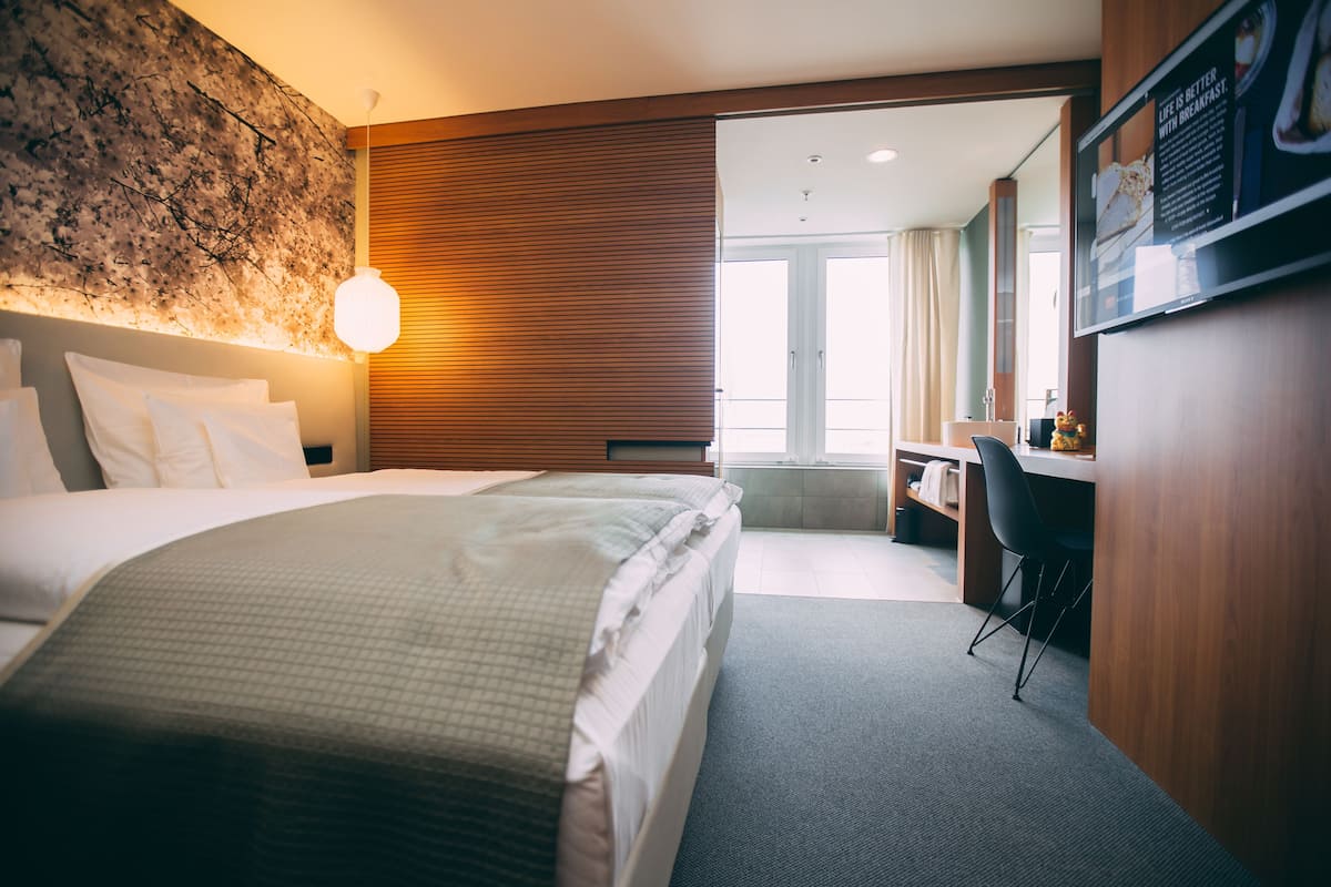 A hotel room with a large bed, a desk, and a view of the city.