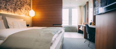 A hotel room with a large bed, a desk, and a view of the city.