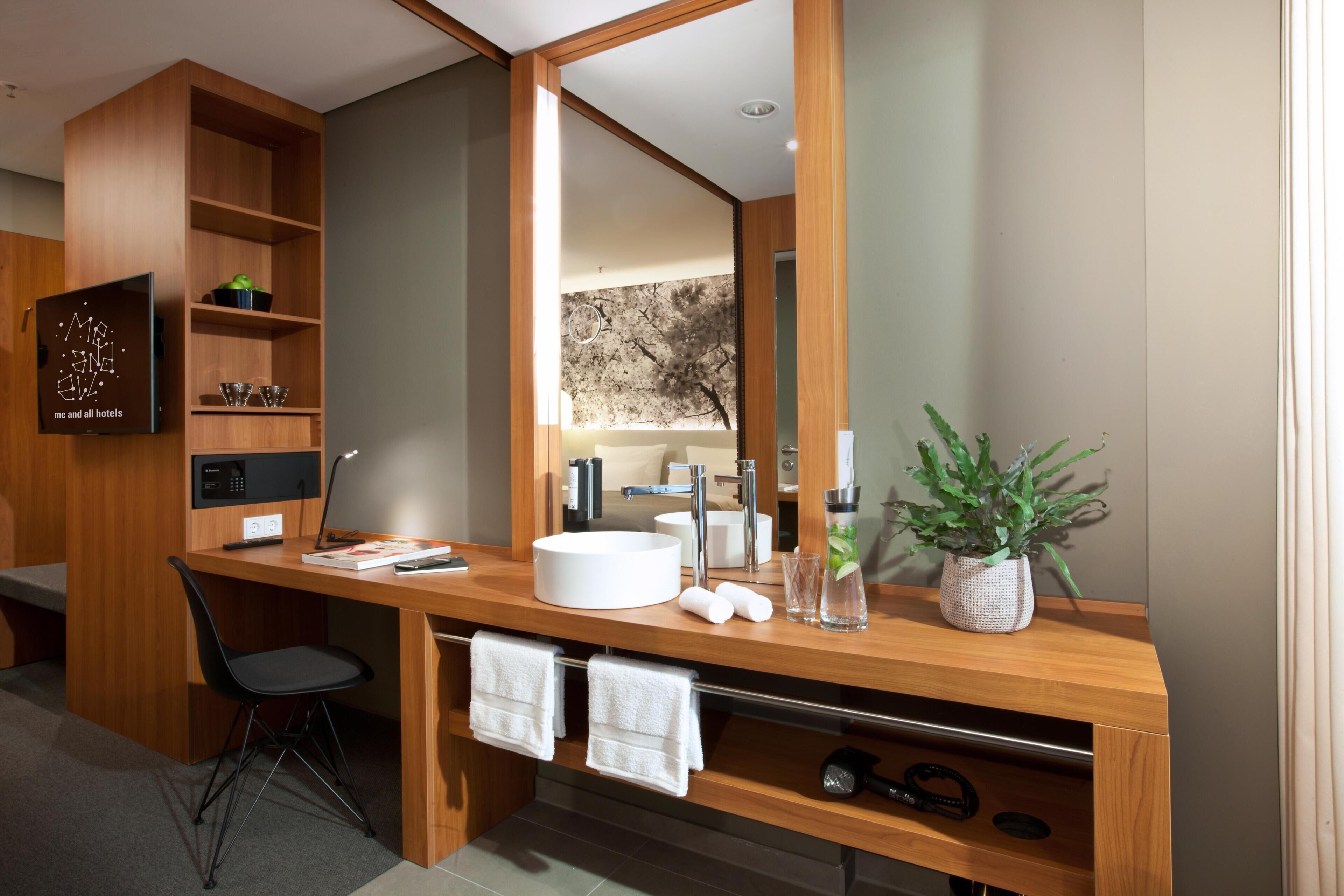 A modern bathroom with a wooden vanity, a large mirror, a round sink, and a potted plant.