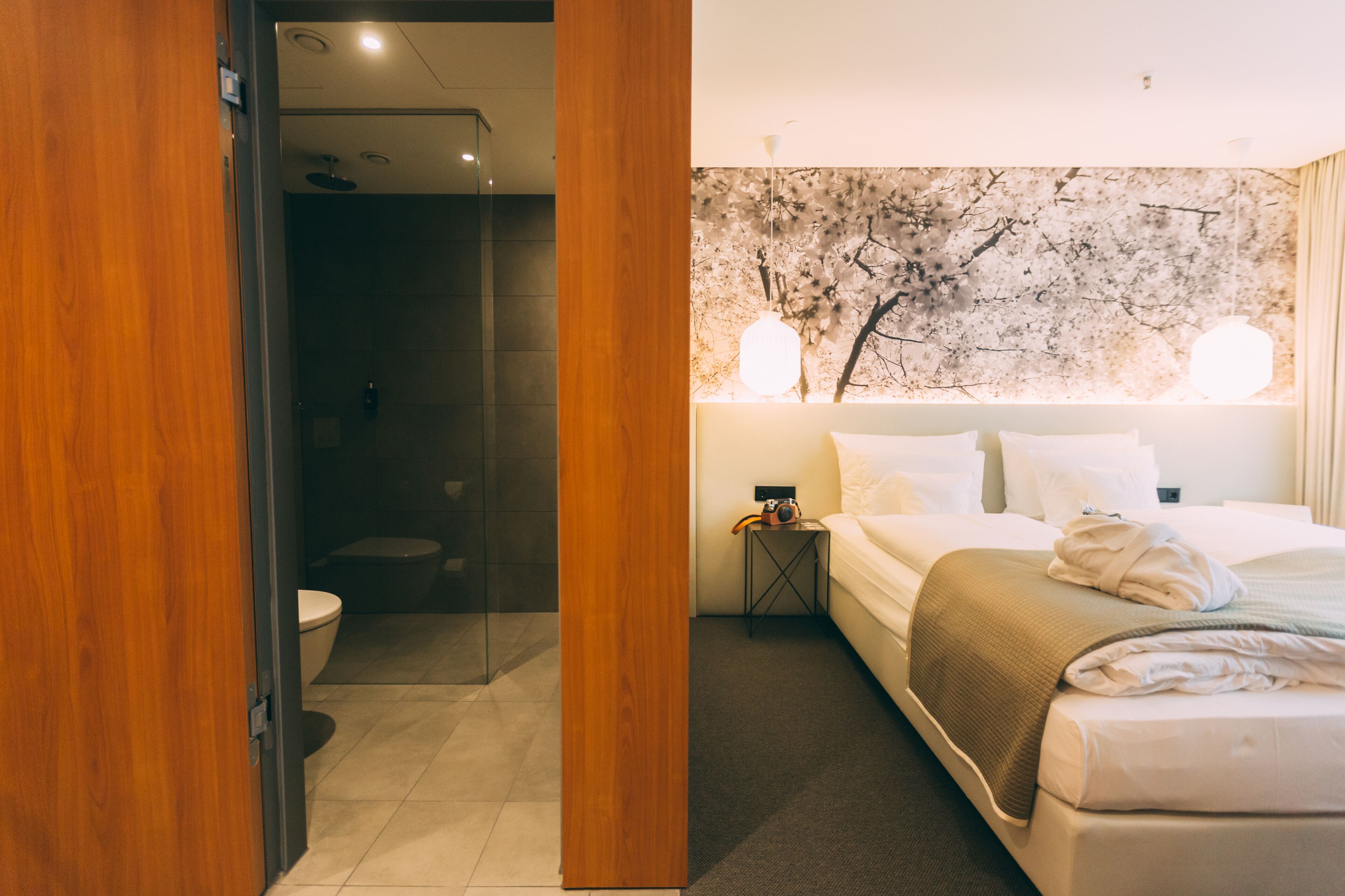 A hotel room with a bed, bedside table, and a wall with a tree mural.