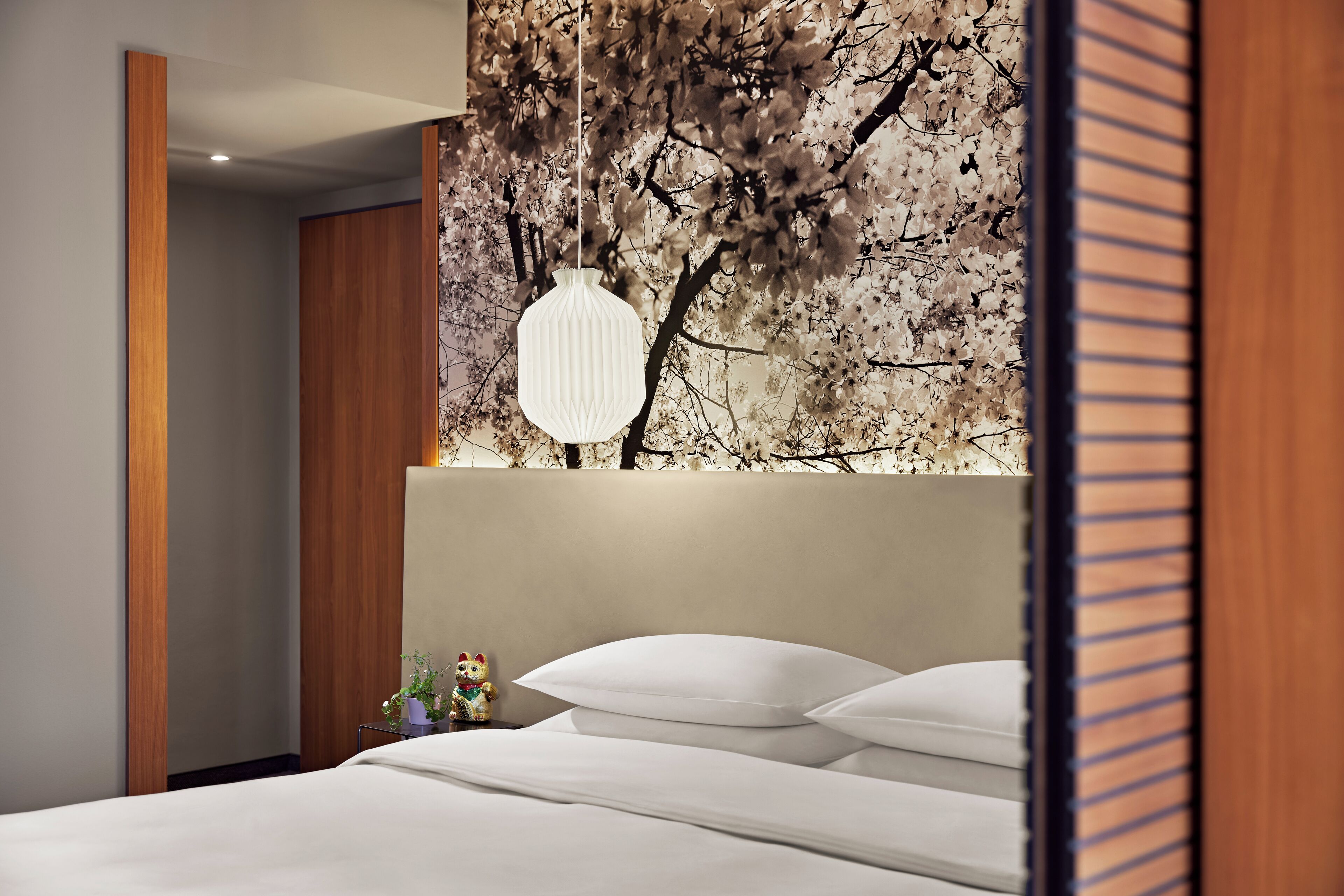 A modern hotel room with a large bed, a decorative wall with a tree design, and a hanging light fixture.