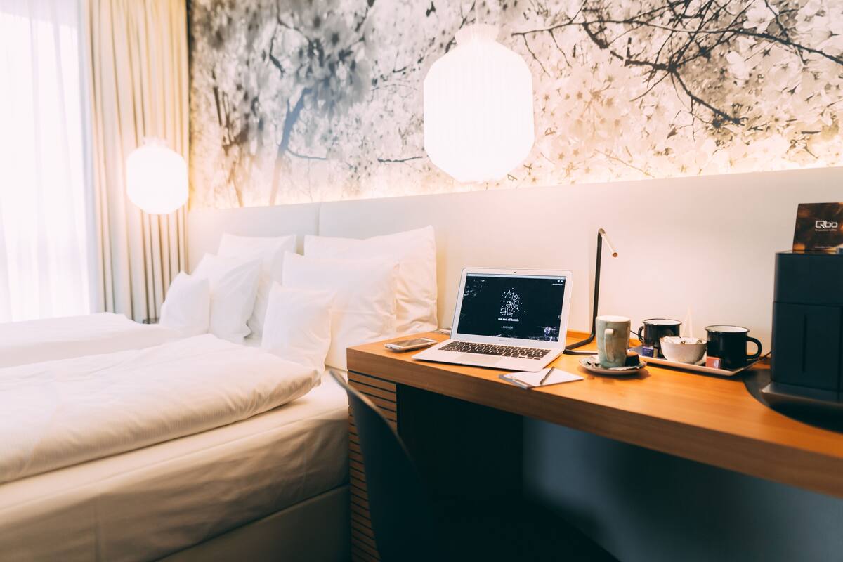 A hotel room with a bed, a desk with a laptop, a coffee maker, and a wall art piece.