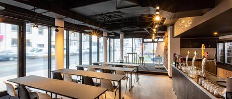 A modern restaurant interior with tables, chairs, a bar area, and large windows.