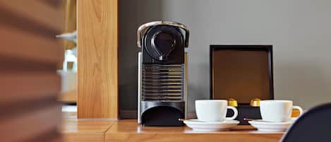 A wooden desk with a coffee machine, two white cups, and a tablet. A clipboard with a QR code is on the wall.
