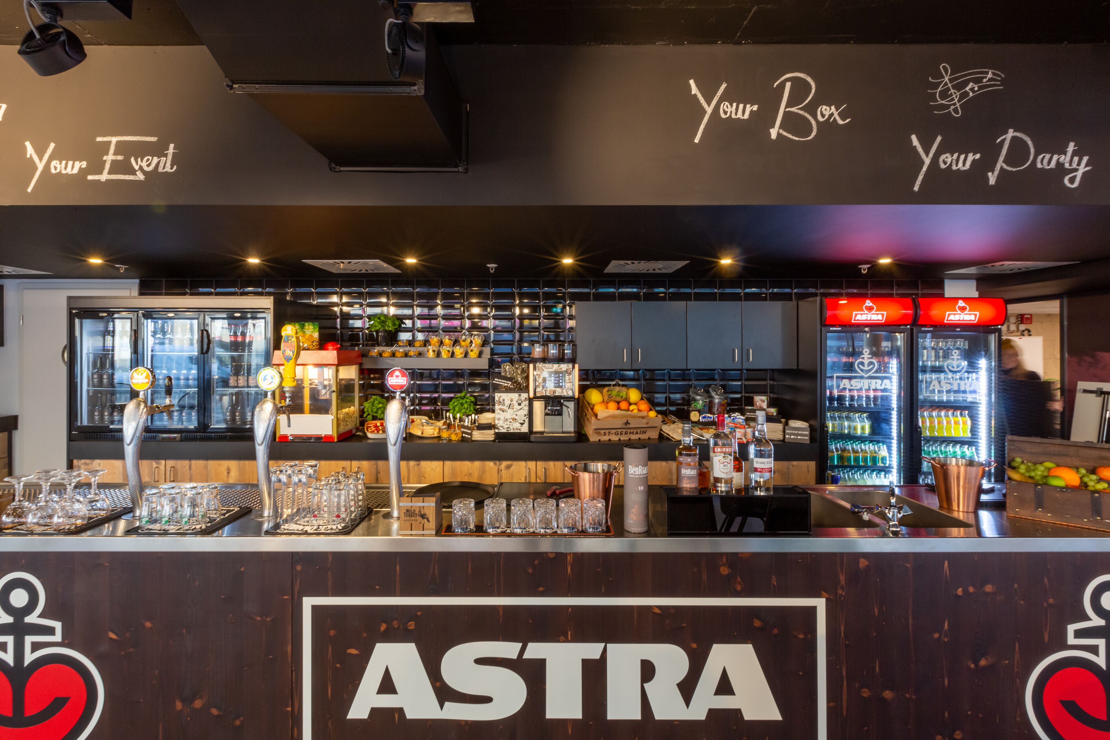 En bardisk med en skylt som visar texten ”ASTRA” och en vägg med texten ”Din plats, din fest”.