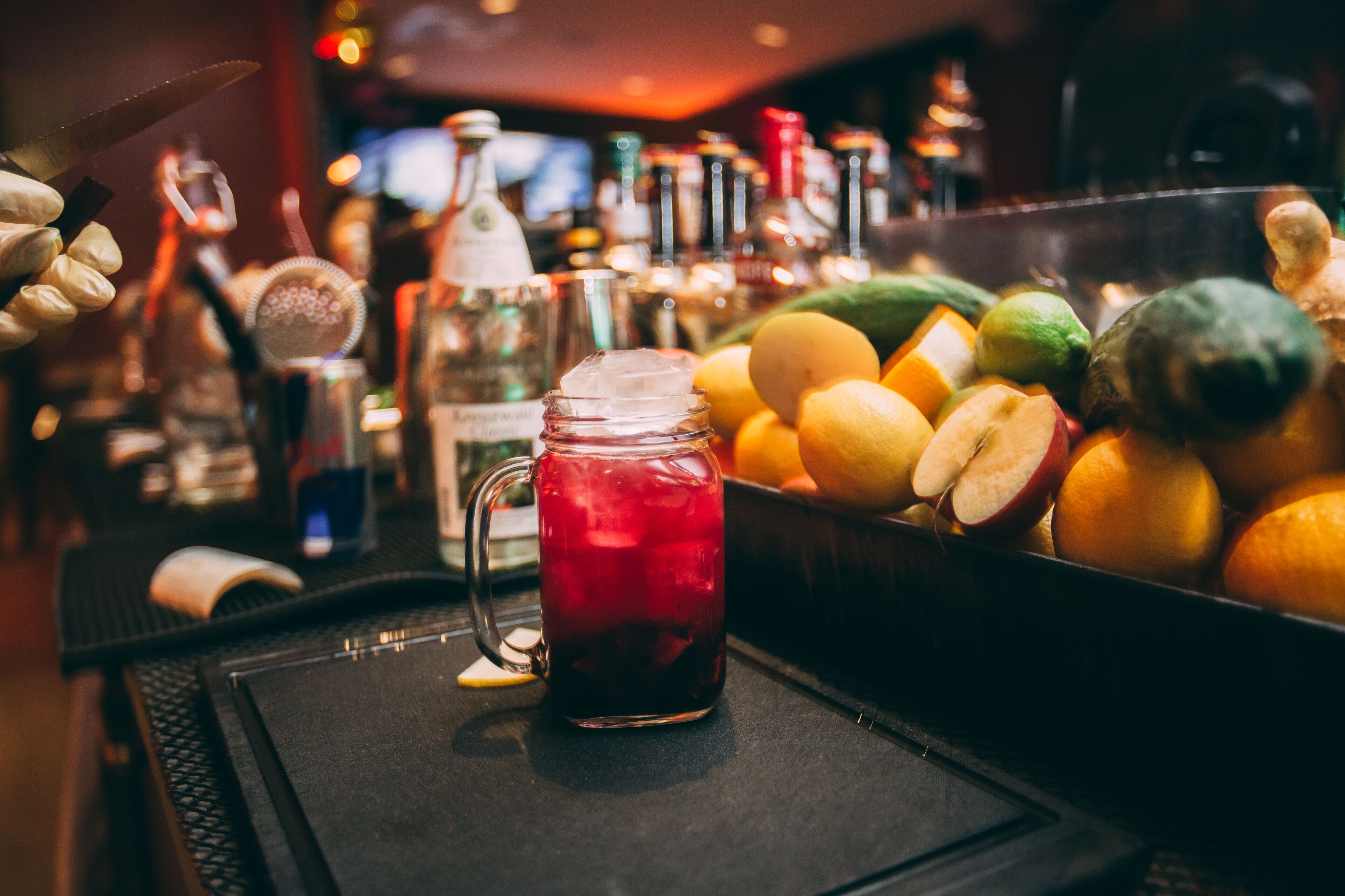 A bar area with a pitcher of red drink, a variety of fruits, and bottles of alcohol.