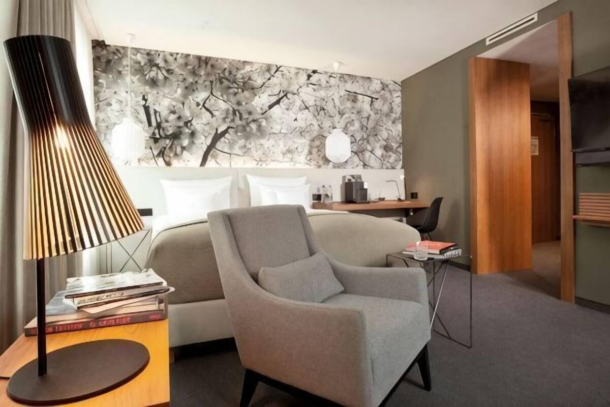 A modern hotel room with a sofa, a lamp, a bookshelf, and a desk.