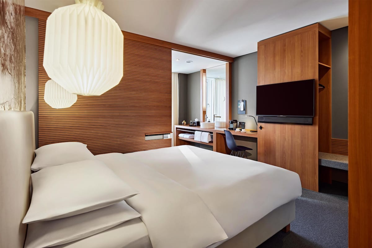 A modern hotel room with a large bed, a desk, a chair, a television, and a mirror.