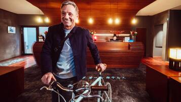 En man på en cykel i en hotellobby med träpanel på väggarna, en receptionsdisk och ett golv täckt av matta.
