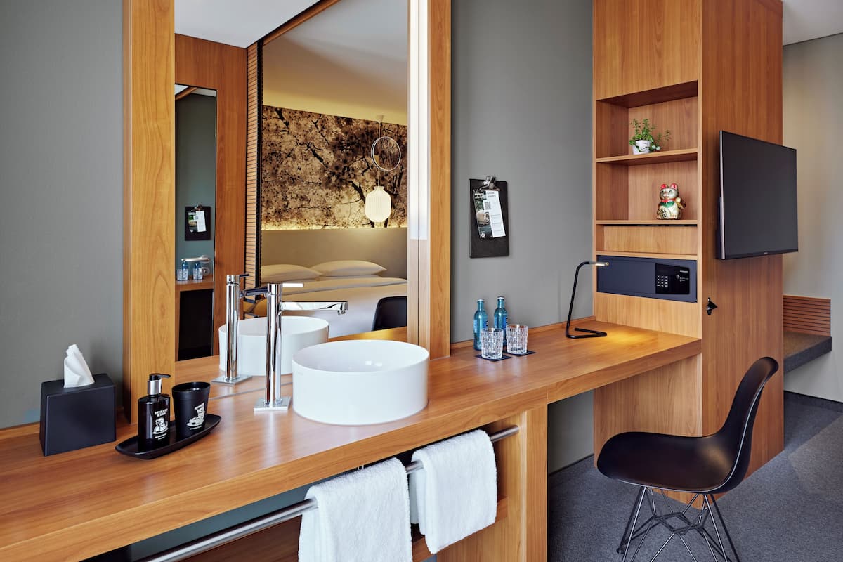 A modern bathroom with a wooden vanity, a large mirror, a white sink, and a black chair.