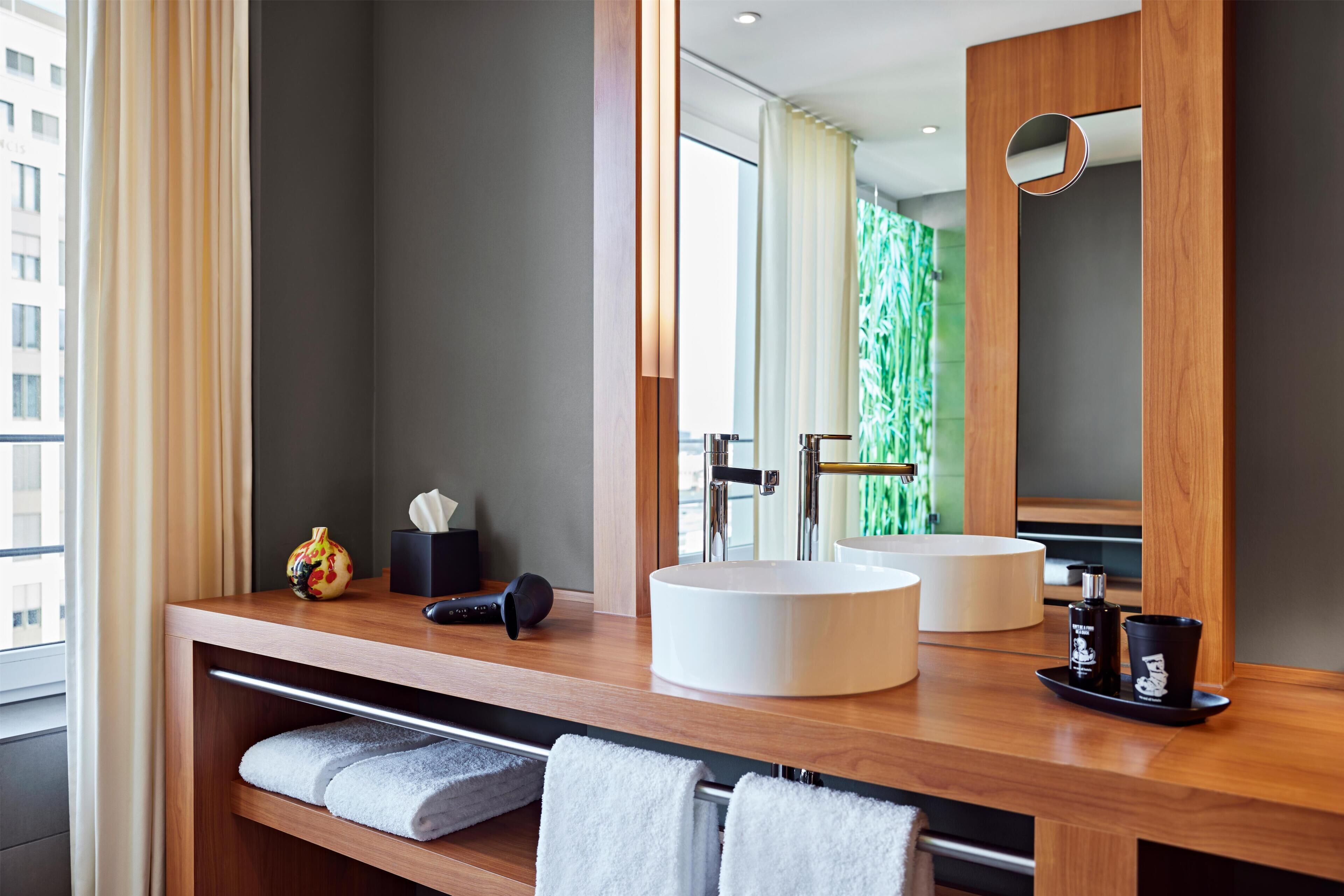 Un baño moderno con tocador de madera, dos lavamanos, un espejo grande y un perchero para toallas.