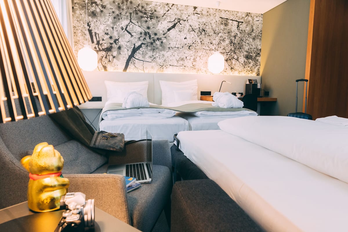 A hotel room with two beds, a sofa, a desk with a laptop, and a decorative lamp.