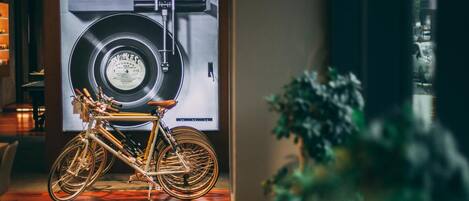 A bicycle in a room with a large vinyl record wall art, wooden flooring, and a plant.