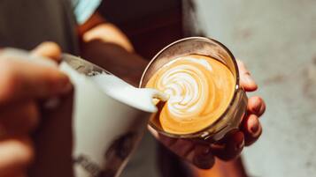 Eine Person hält eine Kaffeetasse mit einem Löffel, eine andere Person eine Tasse, und jemand hält einen Löffel in der Hand.