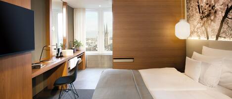 A modern hotel room with a large bed, a desk with a chair, a flat-screen TV, and a city view.