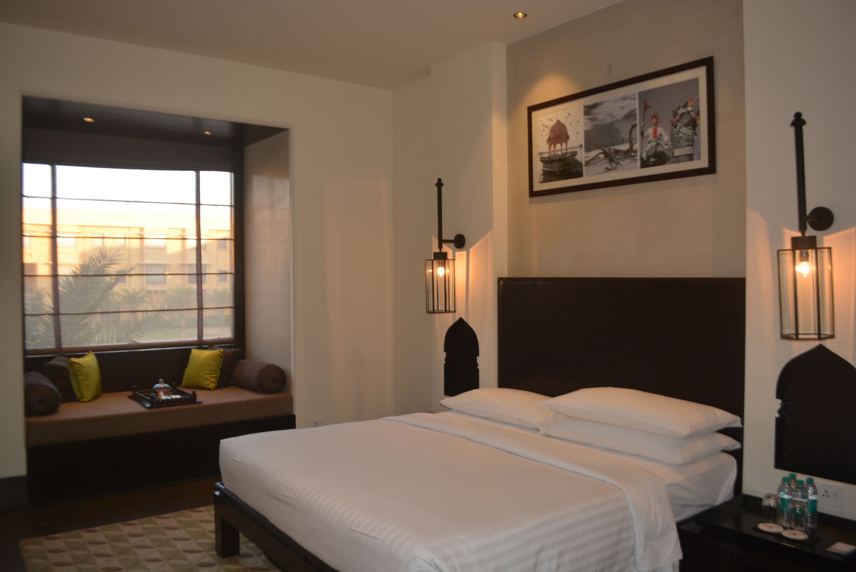 Une chambre d’hôtel avec un grand lit, un coin fenêtre agrémenté de coussins et des lampes fixées au mur.