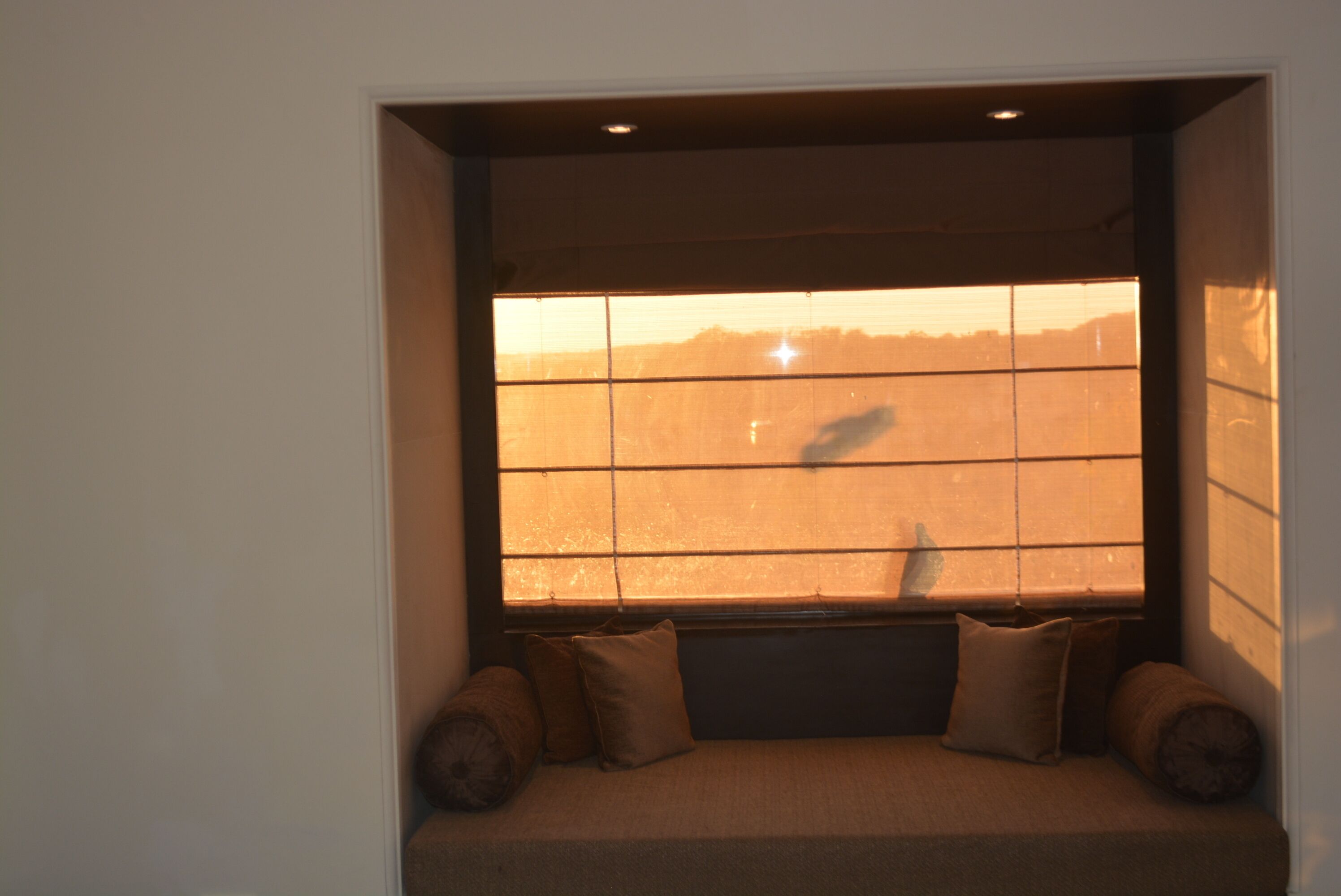 A window seat with a view of a sunset, a cushioned bench, and a small table.