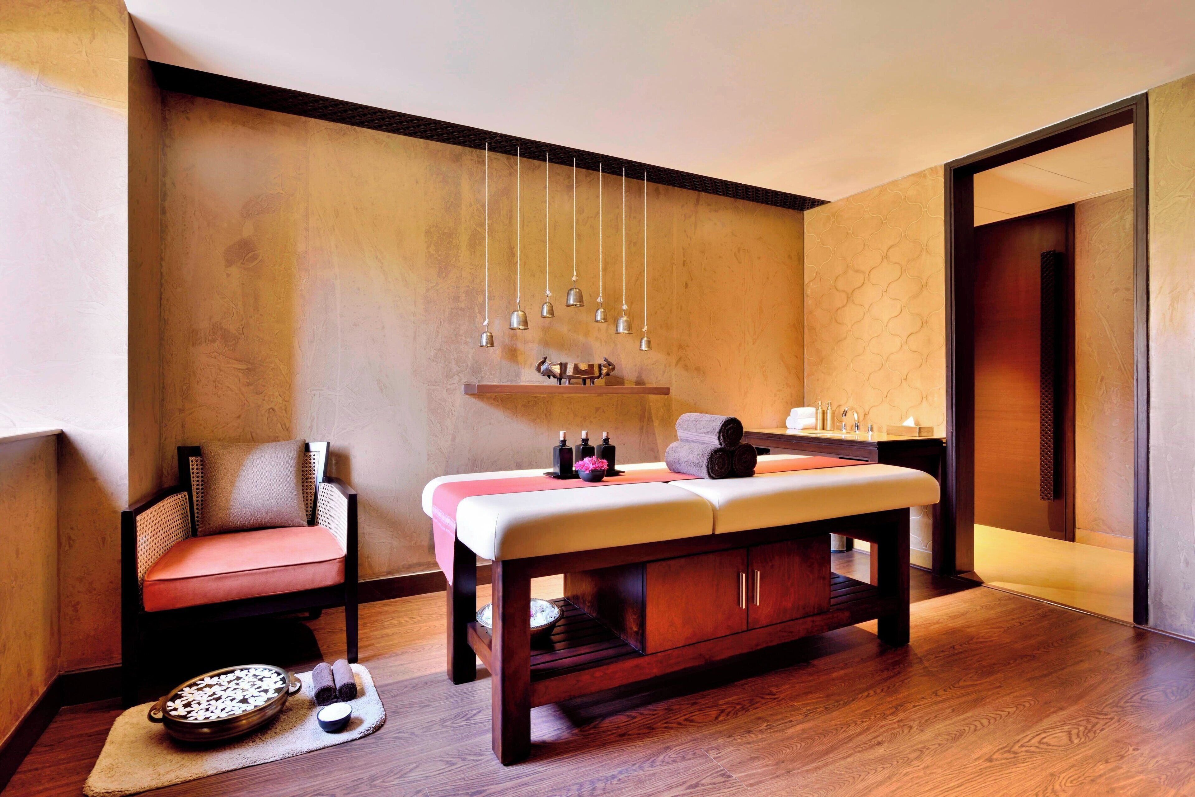 A spa room with a wooden bench, a chair, a massage table, and a wall-mounted sound system.