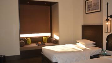A hotel room with two beds, a bench with pillows, a wall-mounted picture, and a bedside table with bottles.