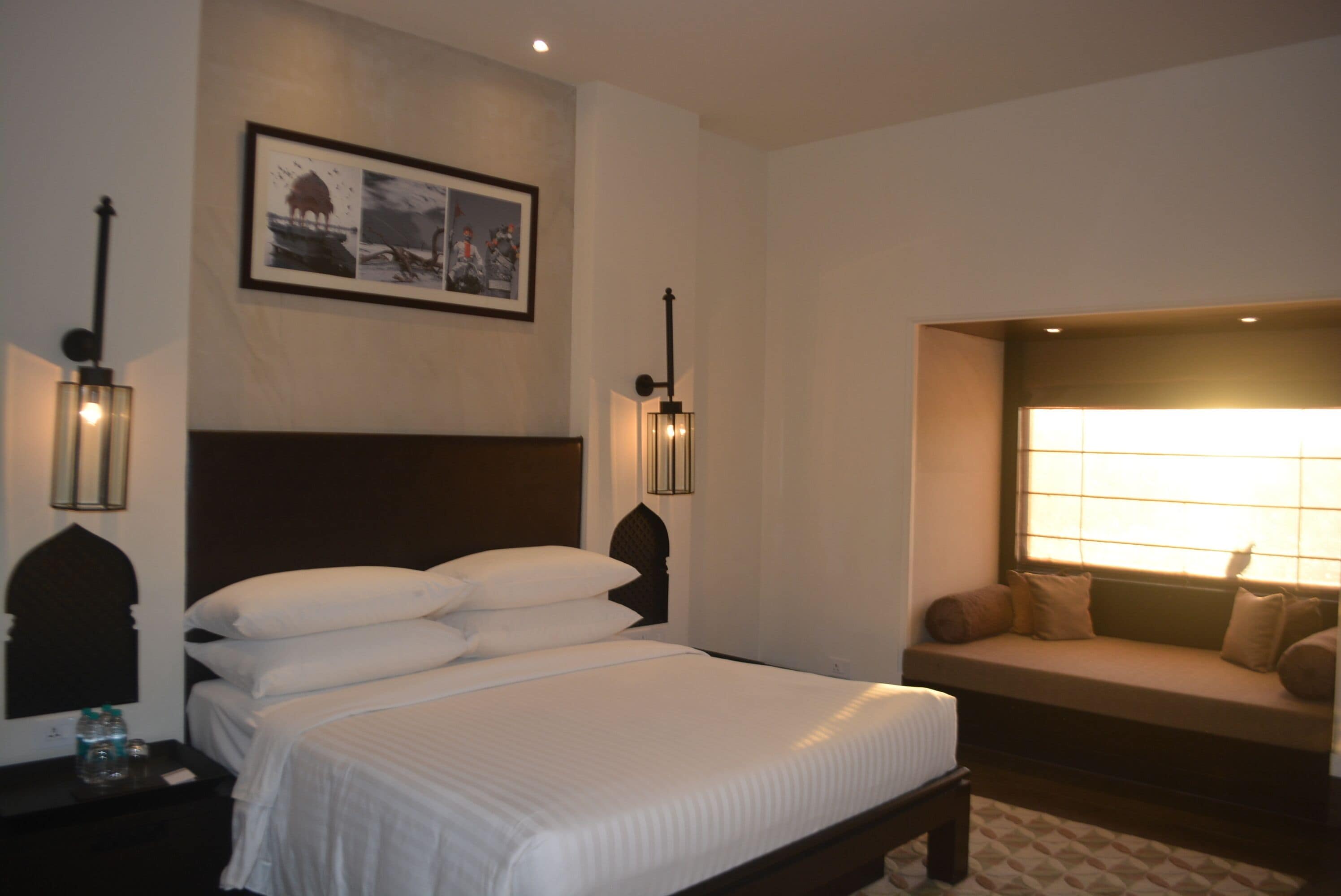 Ein Hotelzimmer mit einem großen Bett, einer Bank am Fenster und Wandleuchten.