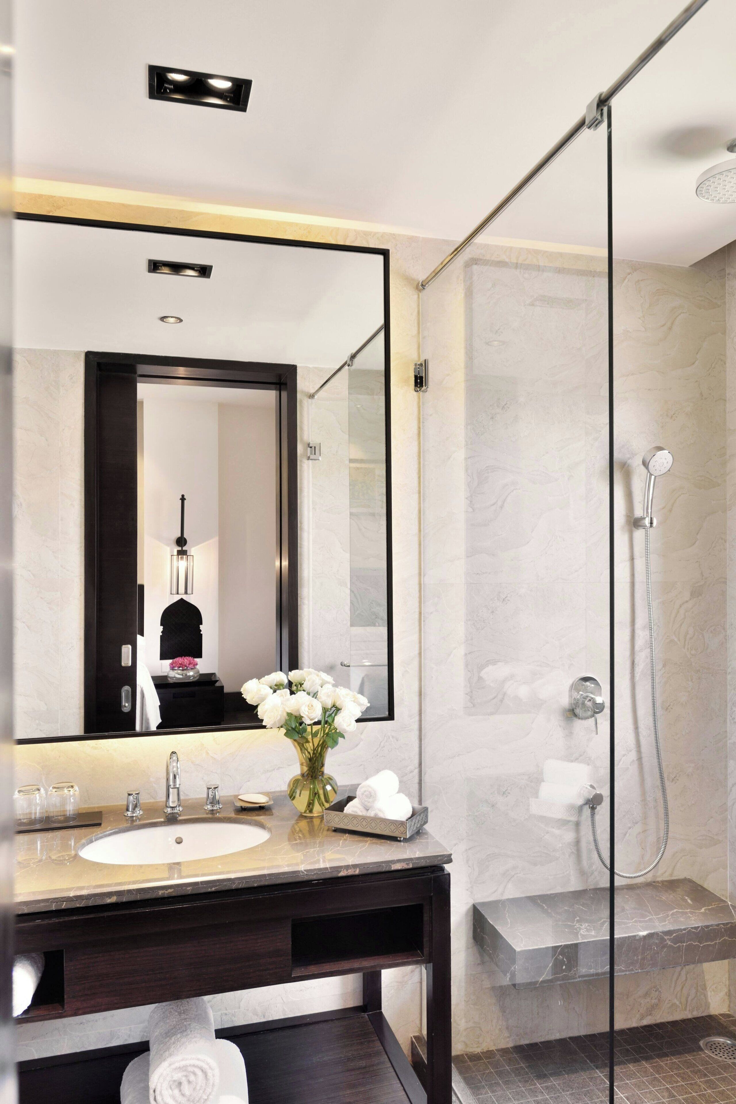 Een moderne badkamer met een grote spiegel, een wastafel, een douche met glazen wanden en een vaas met bloemen.